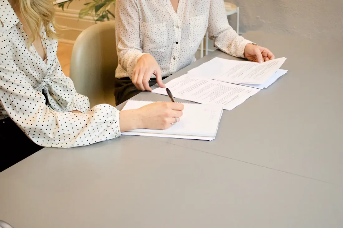 Una mujer firma un documento junto a otra persona